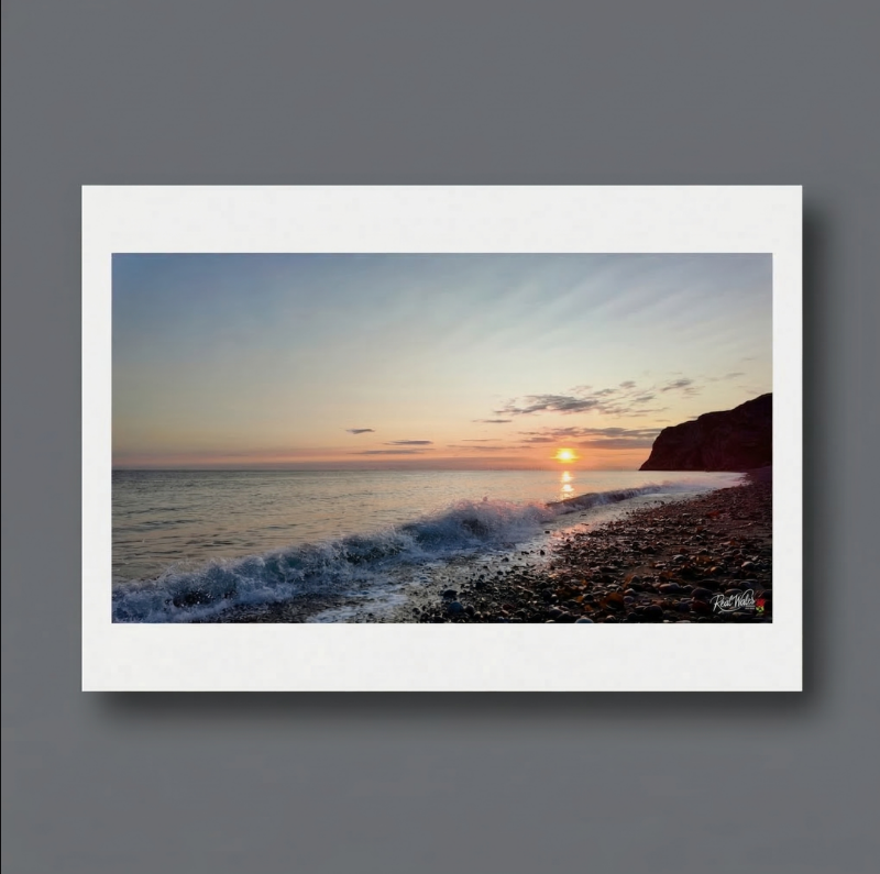 The sweeping shingle beach of Craig-y-Don stretches out to greet the early morning light. Often favoured by locals seeking a quieter, more natural stretch of the bay, this eastern shoreline retains a deeply elemental, coastal charm. Its loose, water-polished pebbles and scattered tangles of fresh kelp offer a raw, textural contrast to the imposing, dark limestone cliffs of the Little Orme rising abruptly at the bay's edge.
