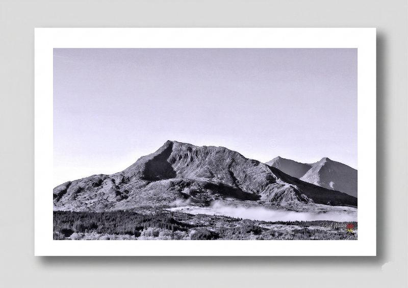 The massive, broad-shouldered silhouette of Moel Siabod rises commandingly above the lush, river-carved valley of the Llugwy. Long celebrated for its isolated, panoramic grandeur and the rugged, boulder-strewn labyrinth of its Daear Ddu ridge, this solitary giant retains a deeply stoic, ancient dignity. Its shifting, silvered flanks of wet scree and the sudden, swirling crowns of cloud that frequently engulf its jagged summit offer a dynamic, restless contrast to the dark, unyielding weight of the vast, hea