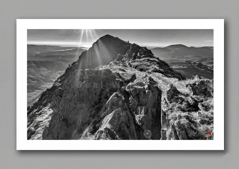 The sharp, pyramidal peak of Cnicht rises dramatically from the rugged expanse of the Moelwynion range, casting a striking, solitary silhouette against the skyline. Long celebrated as the 'Matterhorn of Wales' for its deceptively precipitous profile and the sweeping, glacial curve of the Croesor Valley that lies far below, this iconic summit retains a deeply solitary, commanding elegance. Its shifting, luminous crown of morning mist and the sudden, sweeping shadows cast by fast-moving clouds offer a dynamic