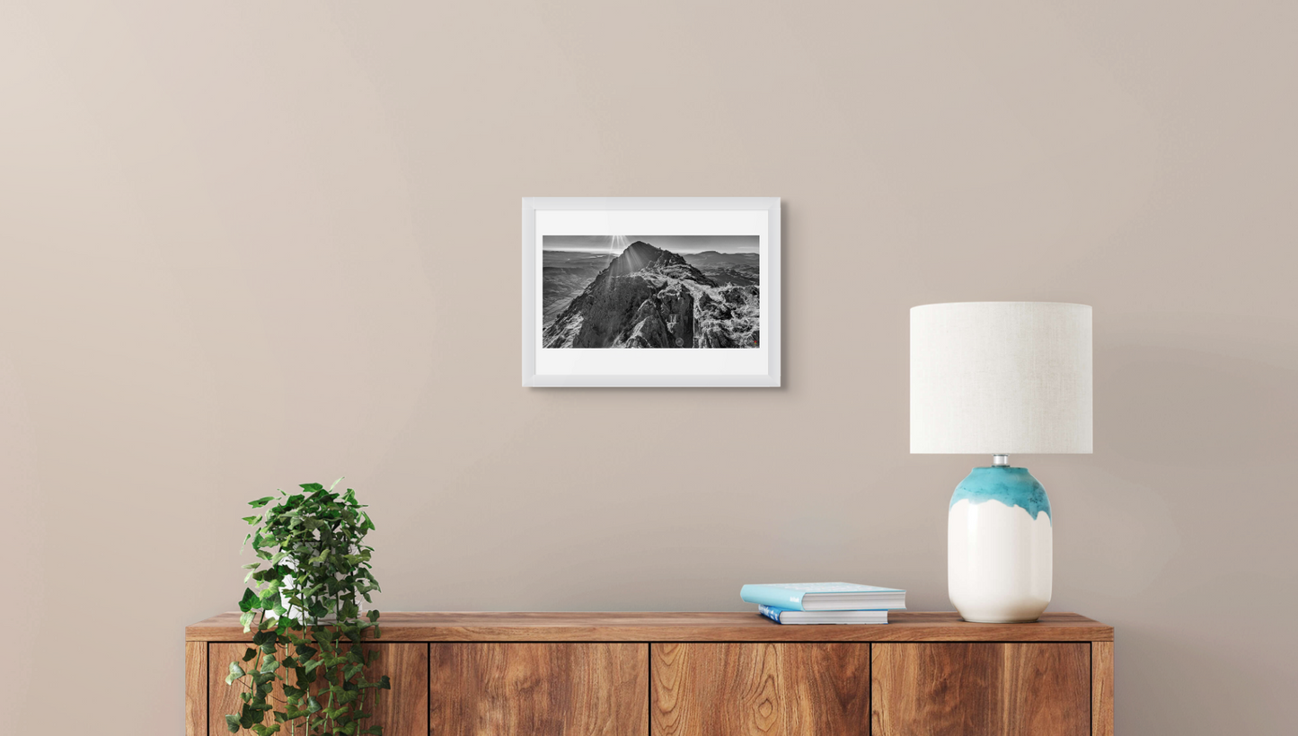 Framed black and white photo on a beige wall above a wooden sideboard with a lamp and books.