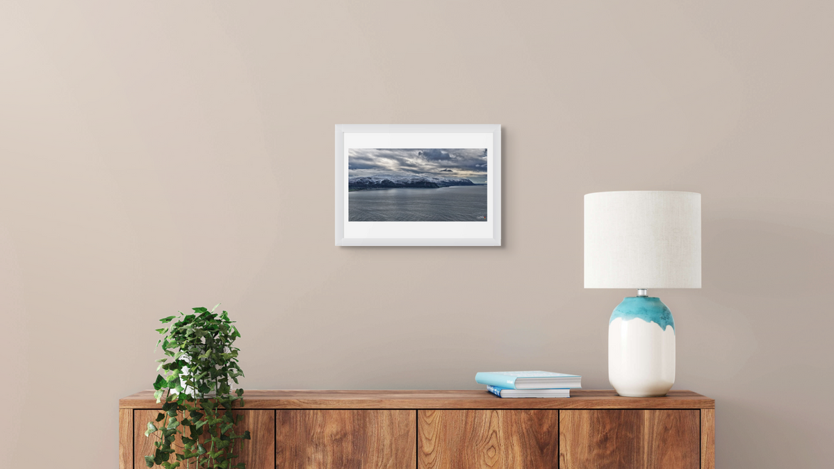 Framed artwork on a wall above a wooden console table with a lamp and books.