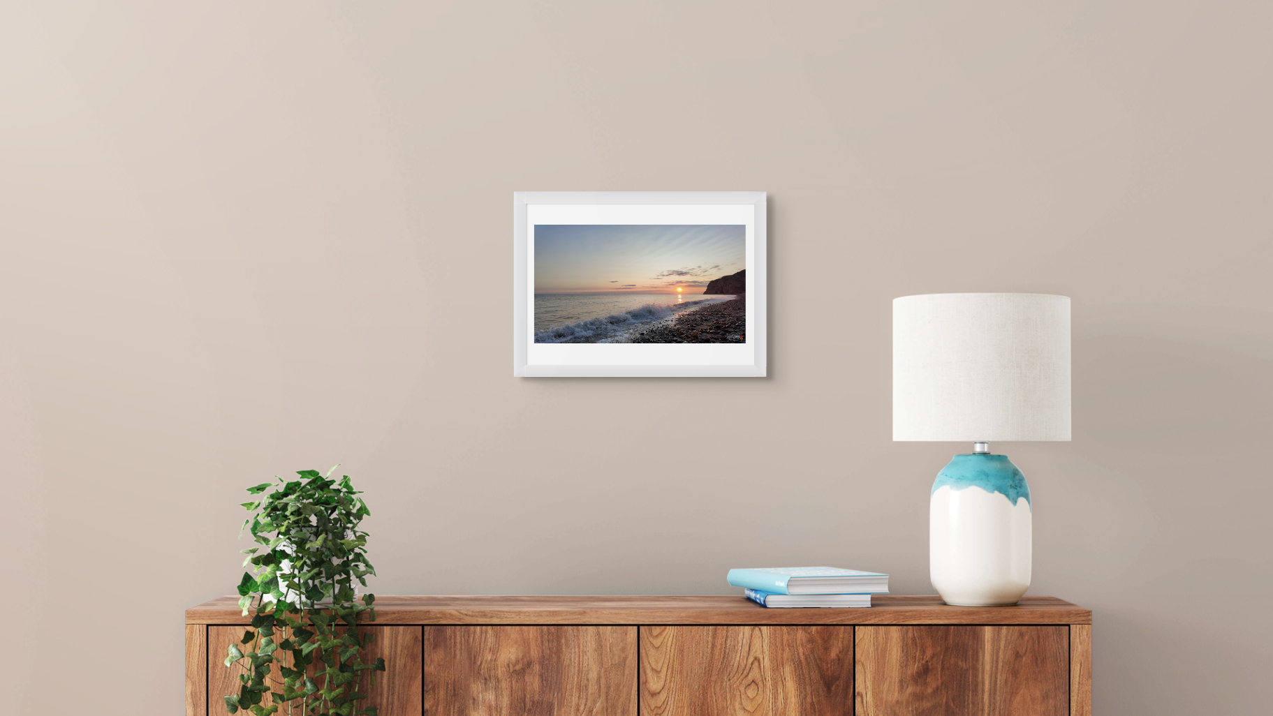 Framed artwork on a wall above a wooden console table with a lamp and plant.