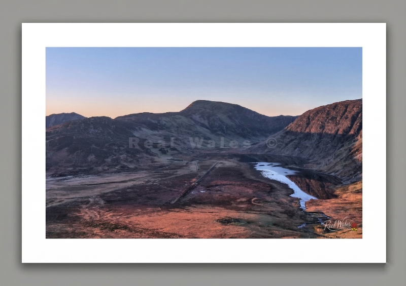 The massive, glacier-hollowed amphitheatre of Cwm Eigiau carves a deep, desolate scar into the eastern flanks of the Carneddau. Long celebrated for its vast, echoing scale and the haunting, broken remains of the Eigiau Dam, a stark monument to the catastrophic flood of 1925, this high, remote basin retains a deeply somber, primordial gravity. Its shifting, water-logged marshlands and the sudden, silver glint of the serpentine streams snaking toward the reservoir offer a dynamic, restless contrast to the dar