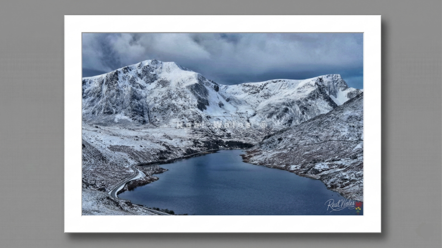 The dark, glacially-scoured trench of Llyn Ogwen lies fiercely trapped between the towering, shattered ramparts of the Carneddau and the Glyderau. Long celebrated for its raw, unforgiving beauty and the looming, monolithic presence of Tryfan guarding its eastern approach, this striking ribbon lake retains a deeply primordial, hostile grandeur. Its shifting, ice-rimmed surface and the sudden, biting squalls that whip across the freezing water offer a harsh, restless contrast to the immense, unyielding weight