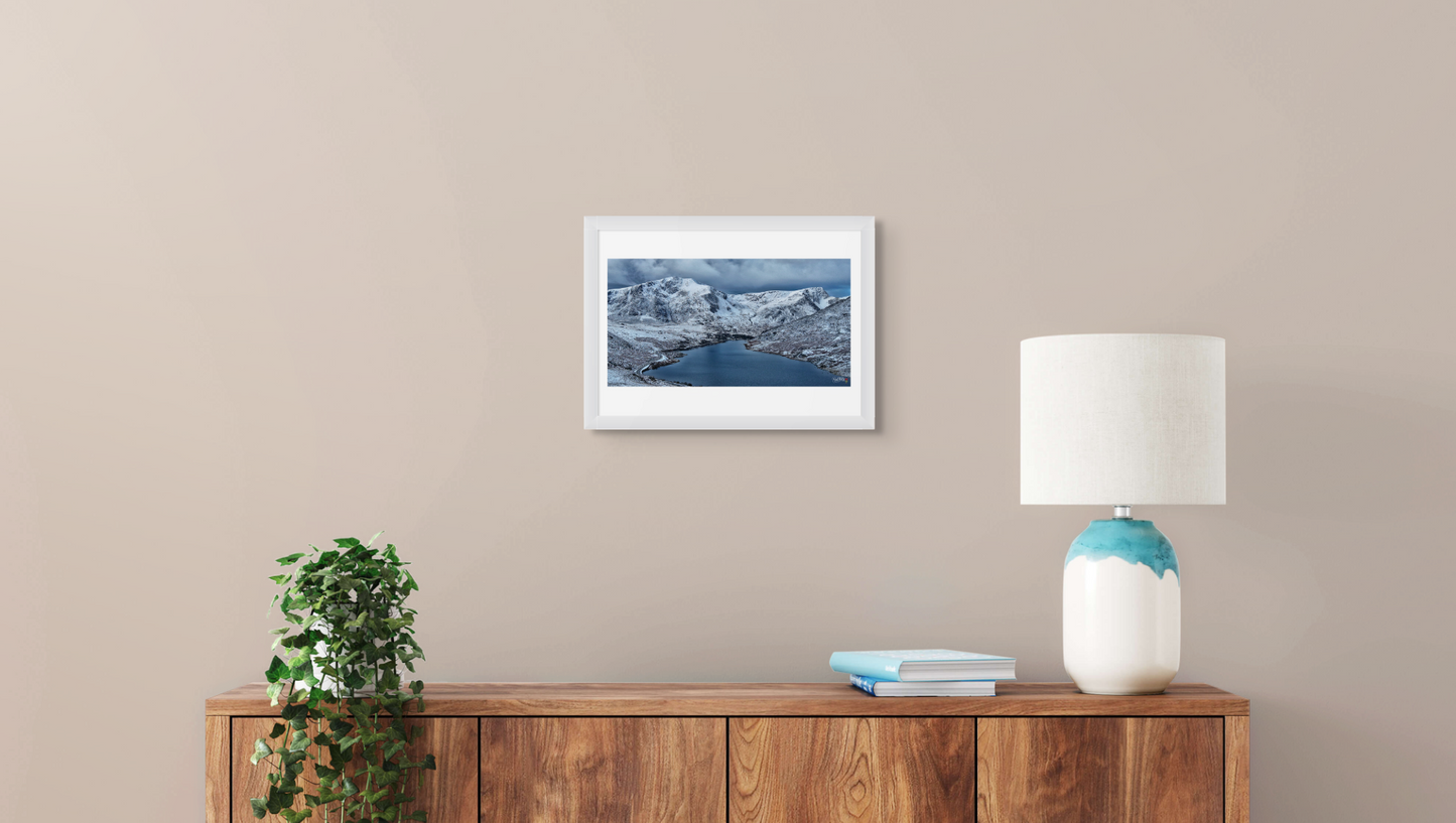 Framed picture on a wall above a wooden console table with a lamp and books.