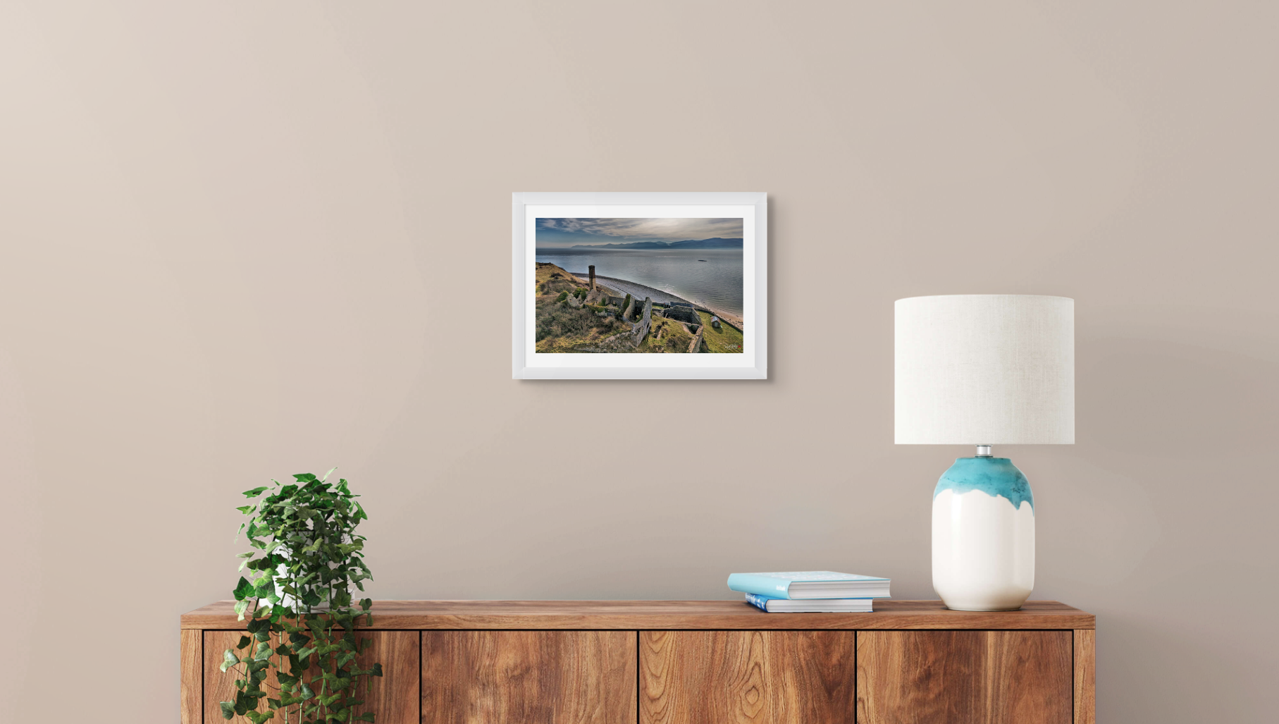 Framed artwork on a wall above a wooden console table with a lamp and books.