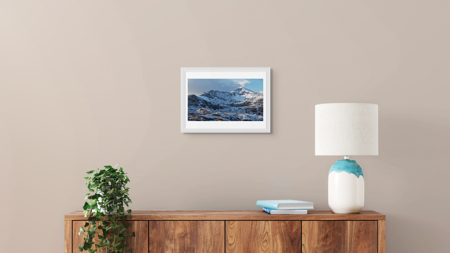 Framed mountain landscape print on a wall above a wooden console table with a lamp and books.