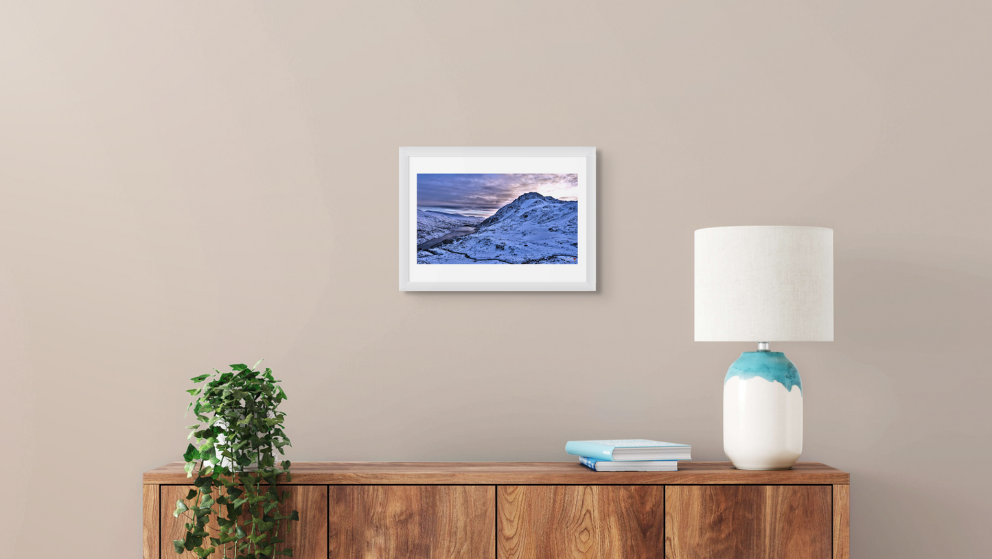 Framed artwork on a wall above a wooden console table with a lamp and plant.