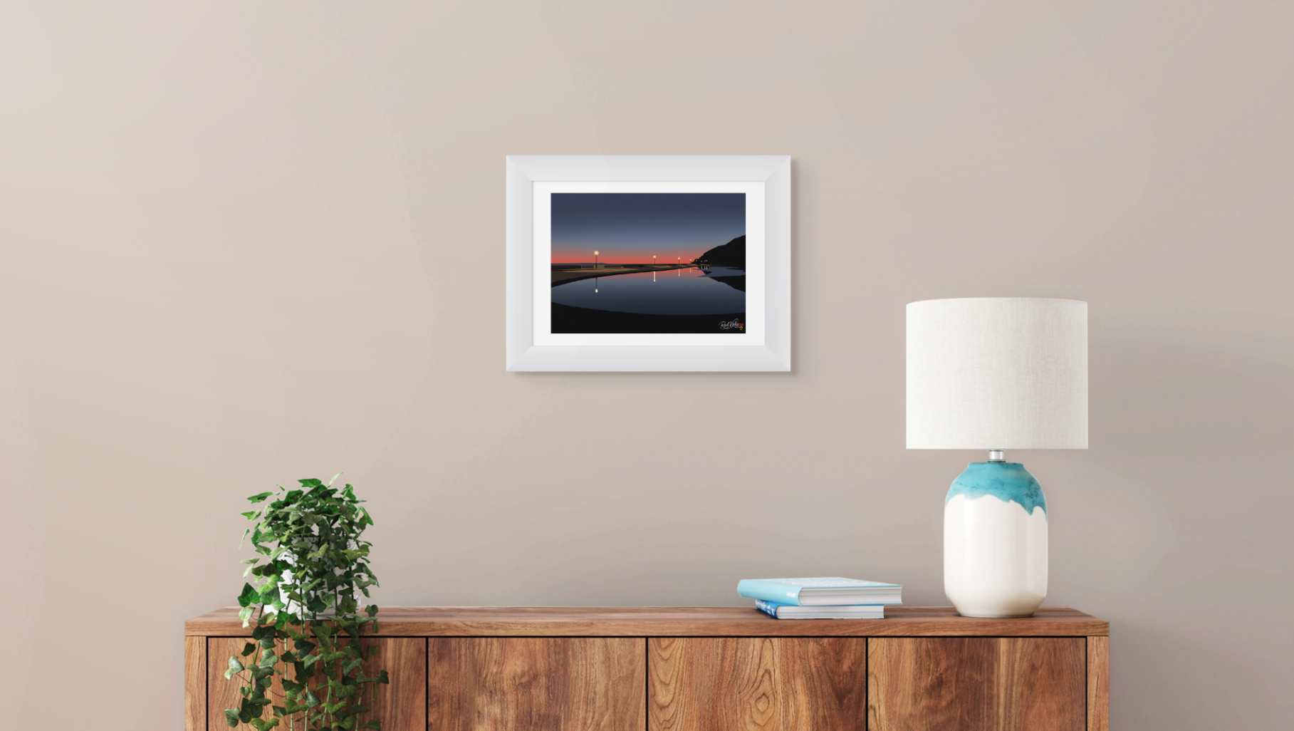 Framed artwork on a wall above a wooden console table with a lamp and books.
