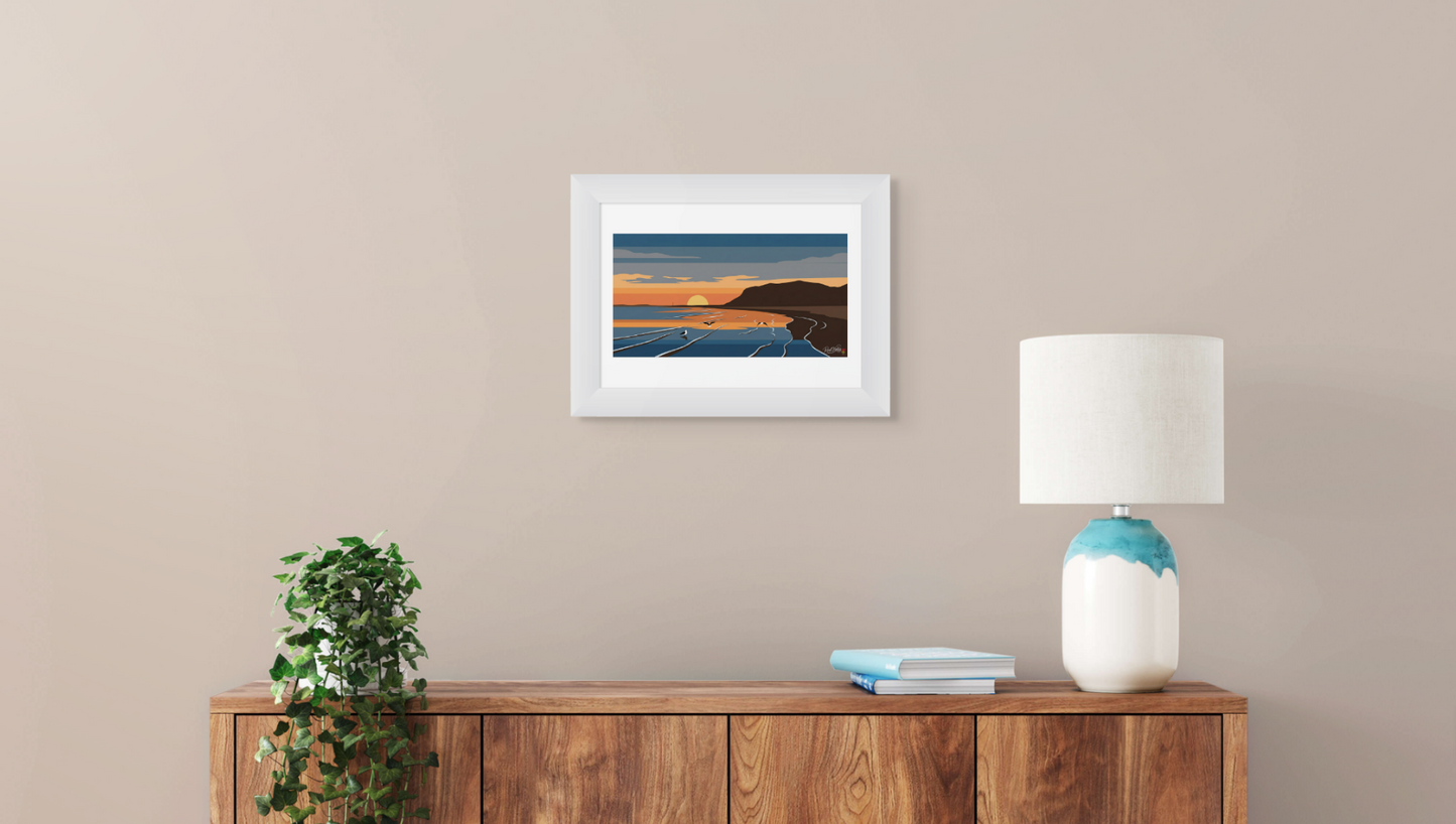 Framed artwork on a wall above a wooden cabinet with a lamp and plant.