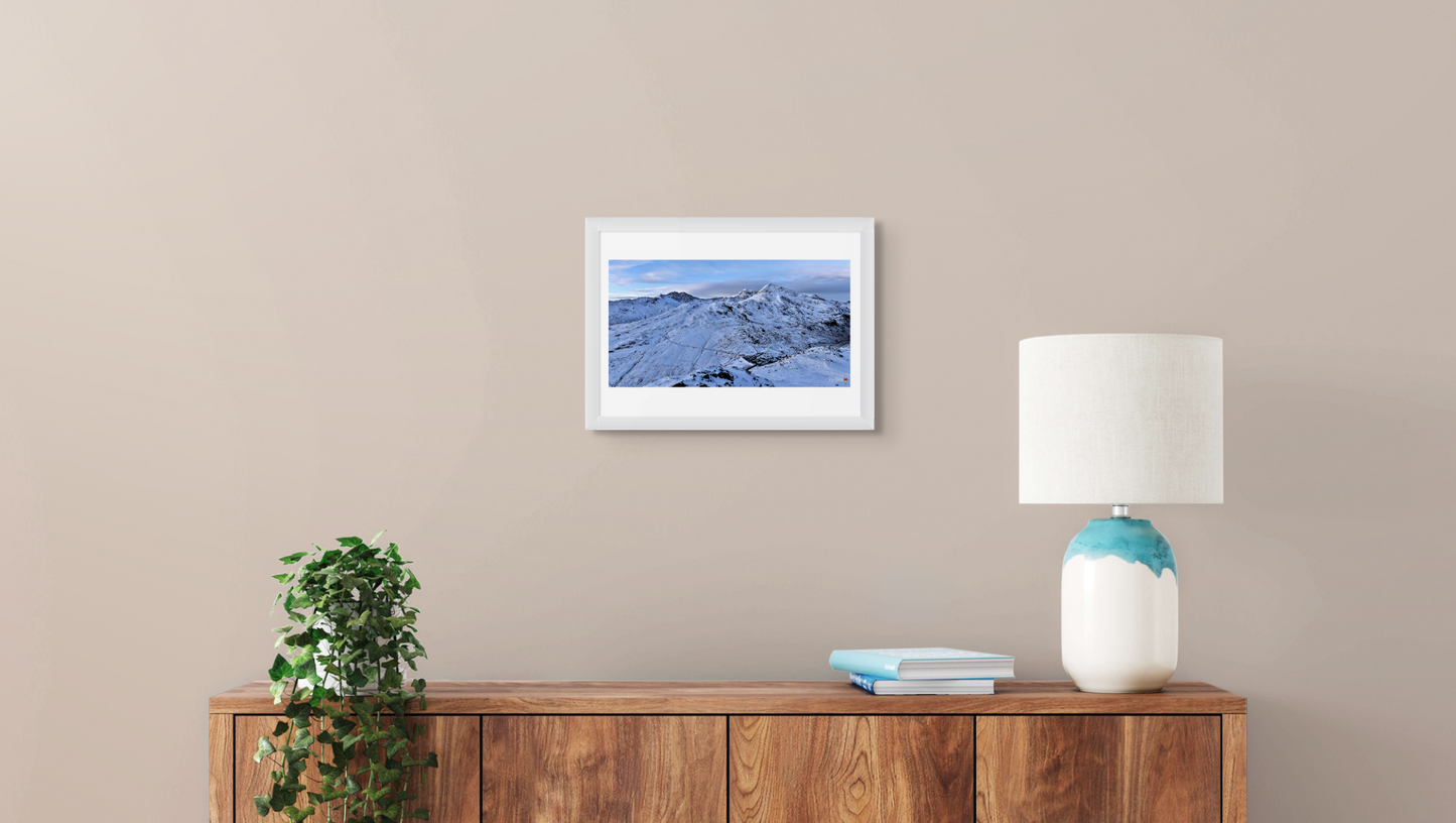 Framed photograph on a wall above a wooden sideboard with a lamp and plant.