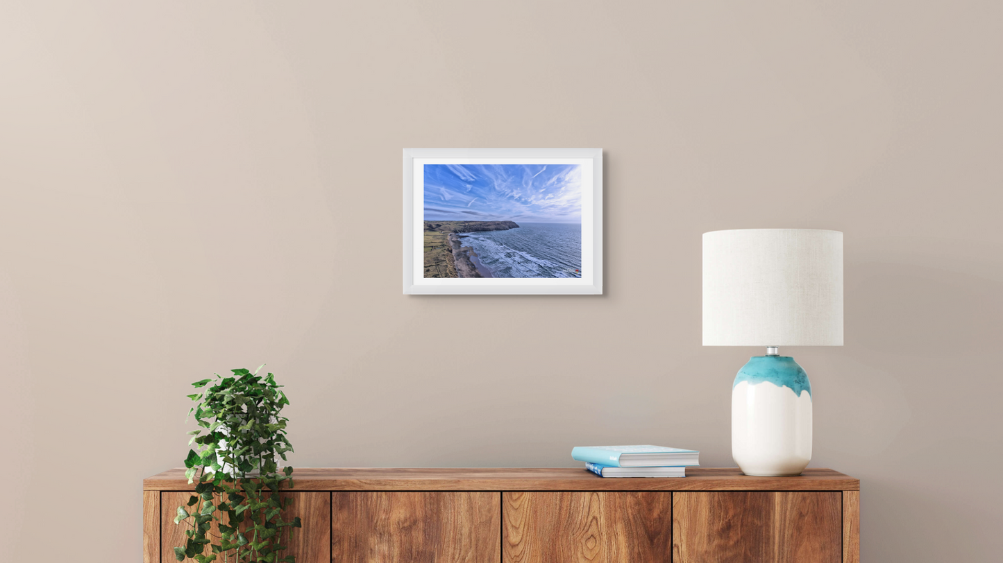 Framed artwork on a wall above a wooden console table with a lamp and books.
